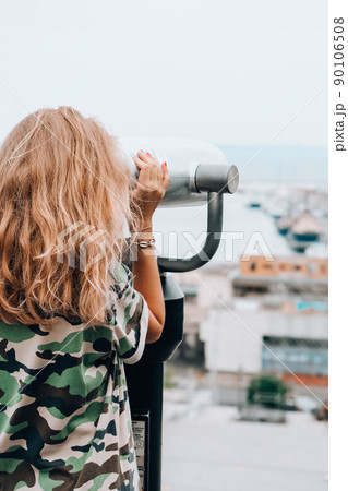 Woman looks through binoculars at the sea. Traveler vacation holiday concept. Using coin operated panoramic telescope Woman looks through binoculars at the sea. Traveler vacation holiday concept. Using coin operated panoramic telescope 90106508