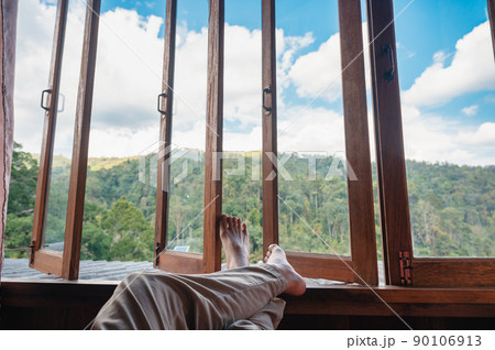 Barefoot man legs relaxing by wooden window in the bedroom and mountain view in countryside 90106913