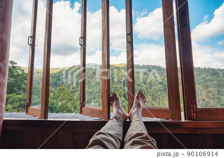 Barefoot man legs relaxing by wooden window in the bedroom and mountain view in countryside 90106914