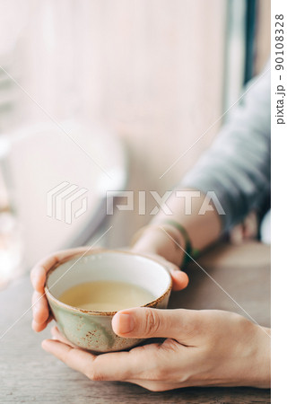 Women's hands hold a cup of tea at a table in a cafe. 90108328