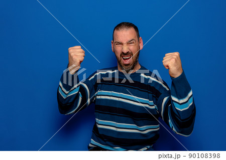 Cheerful excited man in striped pullover standing isolated over blue background, celebrating success. Cheerful excited man in striped pullover standing isolated over blue background, celebrating success. 90108398
