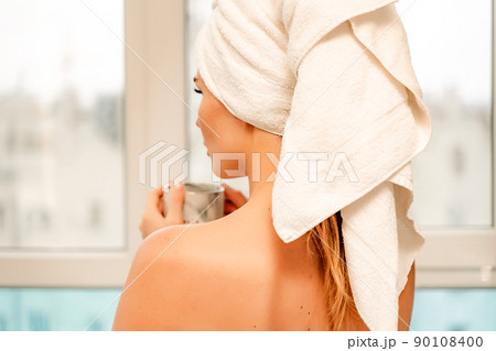 Young serene relaxed woman in spa bath towel drinking hot beverage tea coffee after taking shower bath at home. Beauty treatment, hydration concept. Young serene relaxed woman in spa bath towel drinking hot beverage tea coffee after taking shower bath at home. Beauty treatment, hydration concept. 90108400