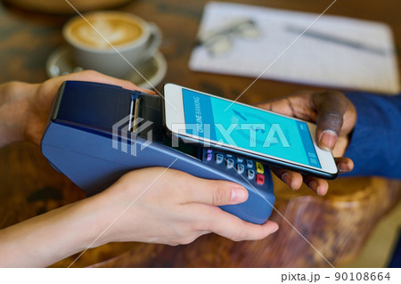 Close-up of customer paying with his mobile phone online while cashier reaching terminal to him 90108664