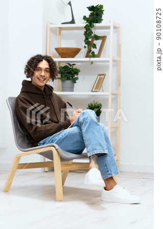 guy with curly hair sit on a chair with a notepad and a writing pen light background 90108725