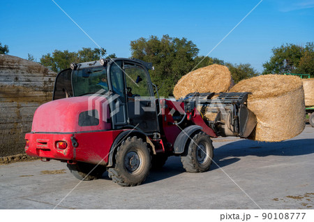 Farmer unloading round bales of straw with a front end loader 90108777