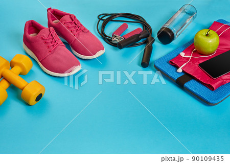 Flat lay of dumbbell, bottle of water, jump rope and sneaker, sport equipments, fitness items, top view 90109435