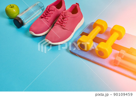 Healthy concept, diet plan with sport shoes and bottle of water and dumbbells on blue background, healthy food and exercise concept. Sun flare 90109459