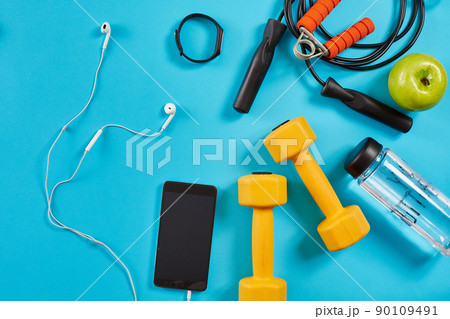 Dumbbells, mobile phone and skipping rope on blue background. Top view. Fitness, sport and healthy lifestyle concept. Dumbbells, mobile phone and skipping rope on blue background. Top view. Fitness, sport and healthy lifestyle concept. 90109491