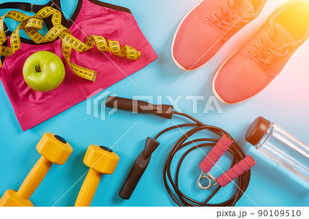 Athlete's set with female clothing, dumbbells and bottle of water on bright blue background. Sun flare 90109510