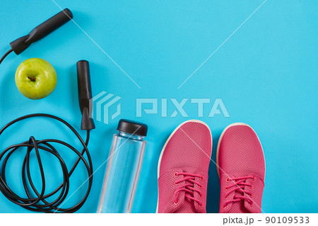 Flat lay of female sport equipments, jump rope, bottle of water and pink sneakers on blue background 90109533