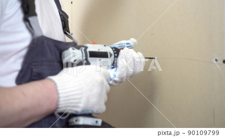 The builder screws the gypsum board with a self-tapping screw using a screwdriver on the wall closeup. The builder screws the gypsum board with a self-tapping screw using a screwdriver on the wall closeup. 90109799