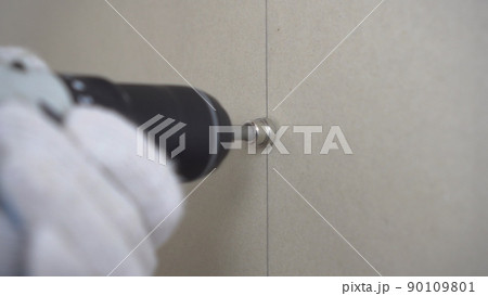 The builder screws the gypsum board with a self-tapping screw using a screwdriver on the wall closeup. 90109801