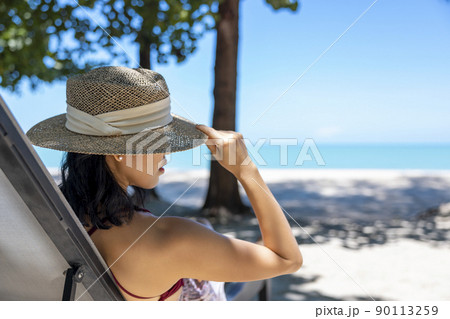 Model Asian woman wearing red swimsuit and straw hat lying on the sun lounger in sun by the sea. Beautiful girl relaxing at infinity luxury resort. Spa, wellness Model Asian woman wearing red swimsuit and straw hat lying on the sun lounger in sun by the sea. Beautiful girl relaxing at infinity luxury resort. Spa, wellness 90113259