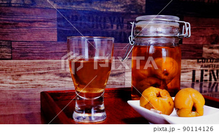 グラスに注いだ手作り梅酒とつまみの漬かった梅　シックな背景 90114126