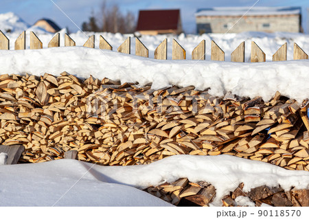 Firewood is stacked in a woodpile along the fence against the blue sky 90118570
