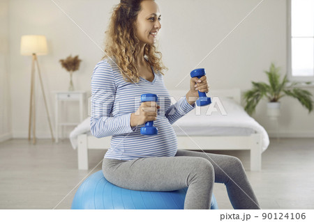 Beautiful and active young pregnant woman with dumbbells and fitball doing sports workout at home 90124106