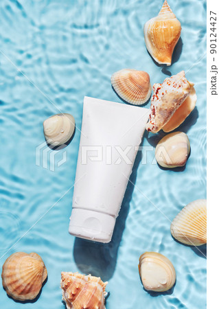 Organic cosmetic product with sea minerals. Skincare treatment cream or sun protection and shells on blue water background 90124427