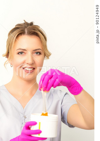 Portrait of a female caucasian beautician holding a jar of sugar paste for sugaring wearing pink gloves on white background Portrait of a female caucasian beautician holding a jar of sugar paste for sugaring wearing pink gloves on white background 90124949
