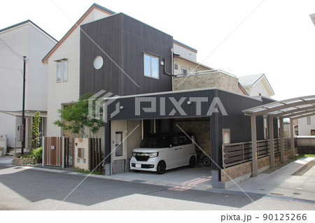 濃い縦板張りのキューブ型と片流れ屋根の淡い外壁と黒いアルミスパンドレルのカーポートが美しい邸宅 90125266