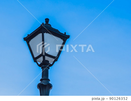 Retro vintage Beautiful forged figured metal black outdoor lamp with glasses, blue clear sky background, copy space. Street lighting equipment, electric savings, power industry, technology. Design 90126352