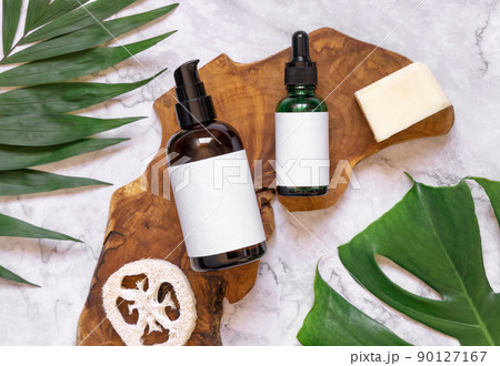 Natural cosmetics in glass bottles on a wooden board near tropical leaves, mockup, top view 90127167