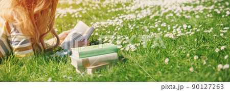Young woman lying on the field and reading some books 90127263