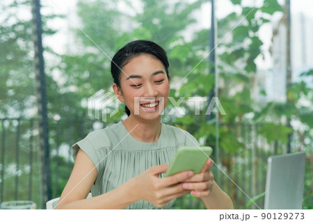 Happy young elegant businesswoman scrolling in smartphone while enjoying break by workplace 90129273