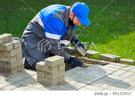 Bricklayer in work clothes sits on sidewalk and lays out paving slabs. Sight of working man in open 90132917