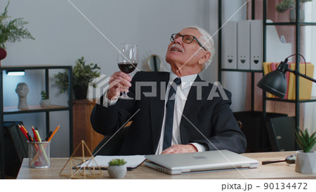 Senior man freelancer drinking wine after working on laptop computer pc sitting at desk at office Senior man freelancer drinking wine after working on laptop computer pc sitting at desk at office 90134472