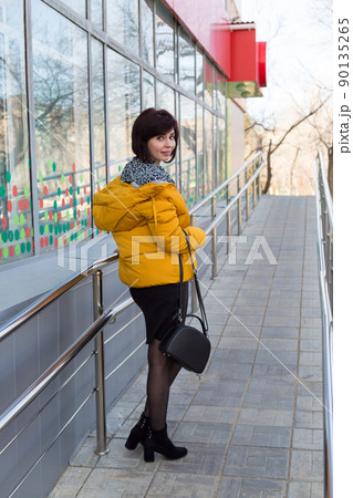 A brunette woman walks through the city with a bright orange jacket on her shoulders, a view from the back A brunette woman walks through the city with a bright orange jacket on her shoulders, a view from the back 90135265