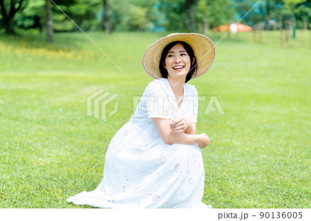 芝生でくつろぐ麦わら帽子の女性 90136005