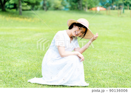 芝生でくつろぐ麦わら帽子の女性 90136006
