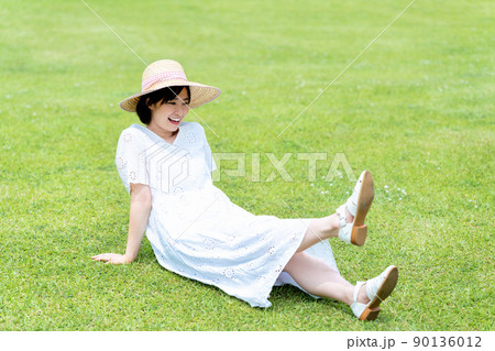 芝生でくつろぐ麦わら帽子の女性 90136012