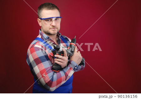 Portrait of a caucasian male repairman in a work uniform with an electric jigsaw around his neck. Studio portrait of an artisan businessman 90136156