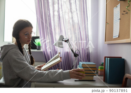 While reading a book at her desk, the girl reached for an apple. While reading a book at her desk, the girl reached for an apple. 90137891
