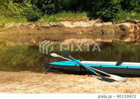 Tourist canoes with paddles stand on the river coast in summer on a water hike. Rafting on inflatable and frame double and triple kayak boats, family trip, extreme adventure in summer Tourist canoes with paddles stand on the river coast in summer on a water hike. Rafting on inflatable and frame double and triple kayak boats, family trip, extreme adventure in summer 90139972