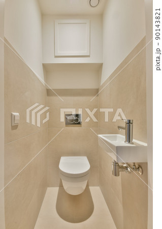 The interior of a bathroom lined with beige tiles in a cozy house with a ceramic sink and a hinged toilet The interior of a bathroom lined with beige tiles in a cozy house with a ceramic sink and a hinged toilet 90143821