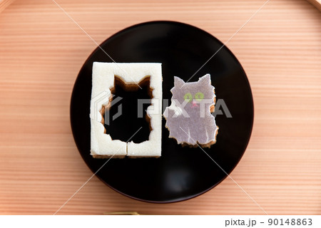 木のお盆と黒い皿に乗った猫の型抜きバウムクーヘン 90148863