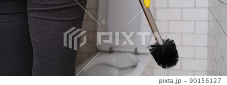 Woman in the toilet holding a brush for cleaning the toilet bowl 90156127