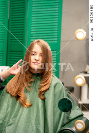 Professional hair care. Young female red-haired with long hair receiving hairstyling in a beauty salon. Professional hair care. Young female red-haired with long hair receiving hairstyling in a beauty salon. 90156369