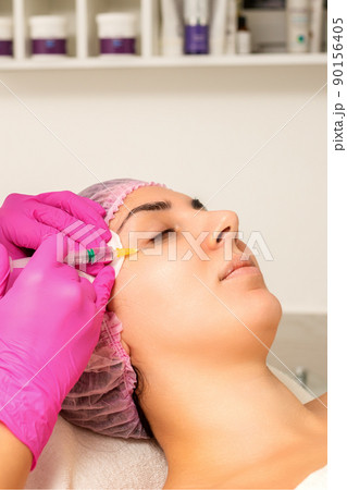 The young white woman is getting rejuvenating facial injections with hyaluronic acid on the eye in a beauty clinic The young white woman is getting rejuvenating facial injections with hyaluronic acid on the eye in a beauty clinic 90156405