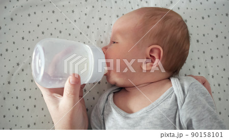 Newborn baby drinks water from plastic bottle lying on bed Newborn baby drinks water from plastic bottle lying on bed 90158101
