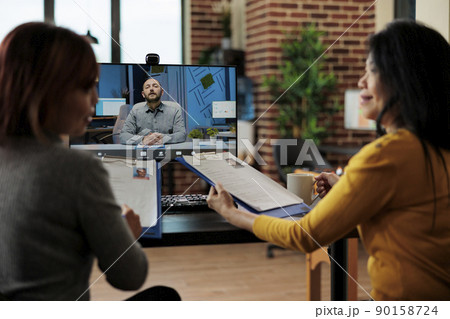 Businesswomen holding clipboard reading recruiter cv discussing company hiring plan during job appointment during online videocall meeting conference in startup office. Teleconference call 90158724
