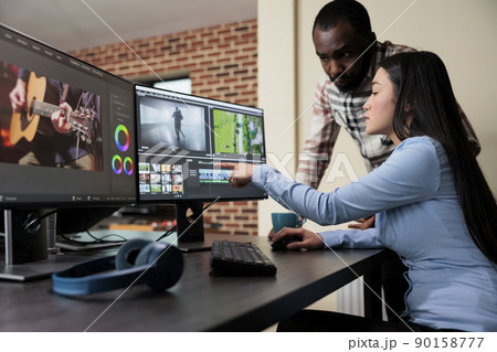 Professional digital movie editor sitting at desk while improving film frames and improving footage quality. Post production house team leader talking with coworker about quality of frames. Professional digital movie editor sitting at desk while improving film frames and improving footage quality. Post production house team leader talking with coworker about quality of frames. 90158777