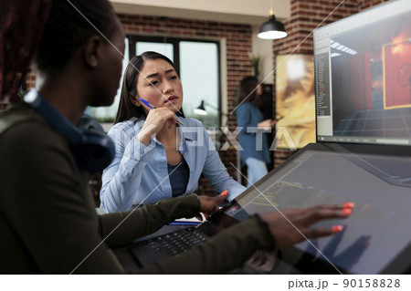 Multiethnic creative game creators sitting at desk with multiple displays while working with 3D assets. Digital interactive entertainment industry workers working with CGI. 90158828