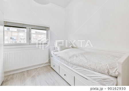 Minimalist interior design of small bedroom with soft bed placed in corner and wooden wardrobe and shelves with lamp illumination 90162930