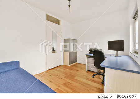 Comfortable chair placed near desk with computer monitors and whiteboard with blue sofa in light workplace in modern apartment 90163007