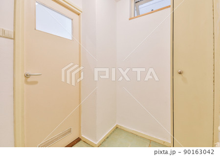 Small corridor with white walls and doors leading to spacious room with narrow wardrobe and parquet floor in modern apartment 90163042