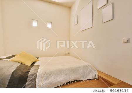 Comfortable low bed placed in small narrow minimalist style bedroom with white walls, pictures and small windows in modern apartment Comfortable low bed placed in small narrow minimalist style bedroom with white walls, pictures and small windows in modern apartment 90163152