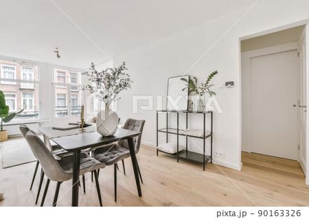 Shabby wooden table with chairs and vase located near comfortable couch against light walls with decorations in modern apartment 90163326